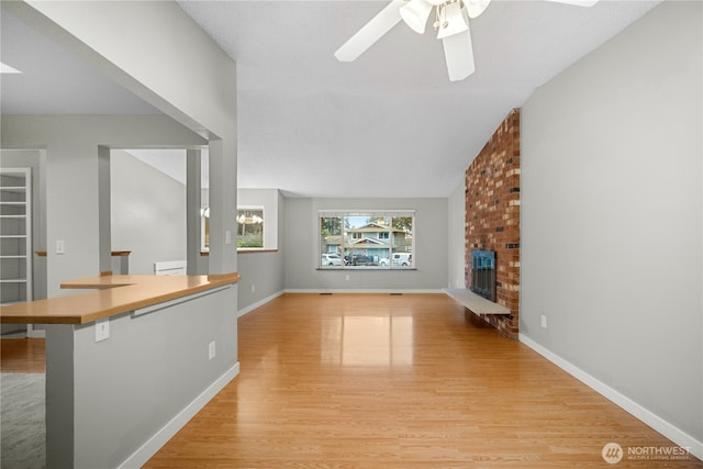 315 Point Fosdick Pl NW, Gig Harbor, WA 98335 - unfurnished living room featuring baseboards, lofted ceiling, light wood-style flooring, ceiling fan, and a brick fireplace