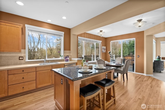 kitchen featuring a breakfast bar, light wood-style floors, a wealth of natural light, and a sink