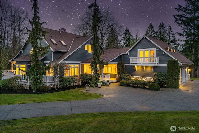 craftsman-style home with stone siding, concrete driveway, an attached garage, a front yard, and a balcony