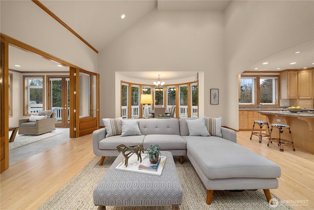 living area featuring a chandelier, a healthy amount of sunlight, high vaulted ceiling, and light wood-style floors