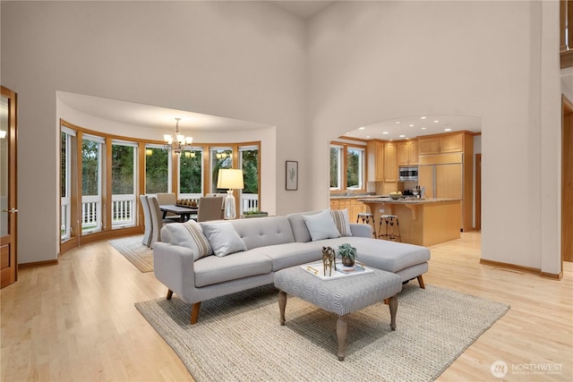 living area with a notable chandelier, baseboards, a high ceiling, and light wood-style floors