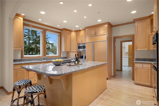 kitchen featuring a breakfast bar, a kitchen island, crown molding, built in appliances, and light stone countertops