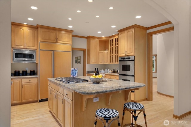 kitchen with light wood-type flooring, a center island, glass insert cabinets, built in appliances, and light stone countertops