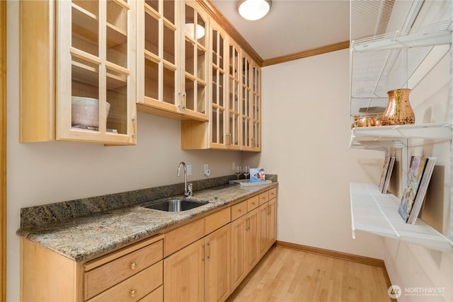 kitchen with light wood-type flooring, ornamental molding, light brown cabinetry, a sink, and baseboards