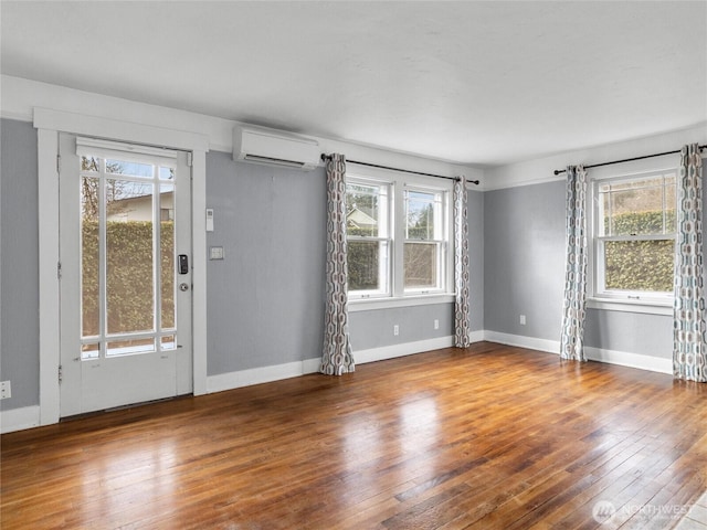 spare room with baseboards, a healthy amount of sunlight, hardwood / wood-style floors, and a wall mounted AC