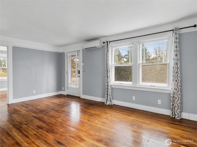 unfurnished room with a wall mounted air conditioner, baseboards, and wood-type flooring