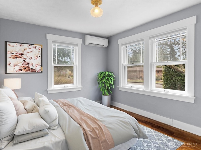 bedroom with baseboards, multiple windows, wood finished floors, and a wall unit AC