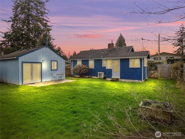 back of house at dusk featuring an outbuilding, fence, a lawn, and a chimney