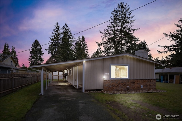 exterior space with fence, a yard, a chimney, a carport, and aphalt driveway