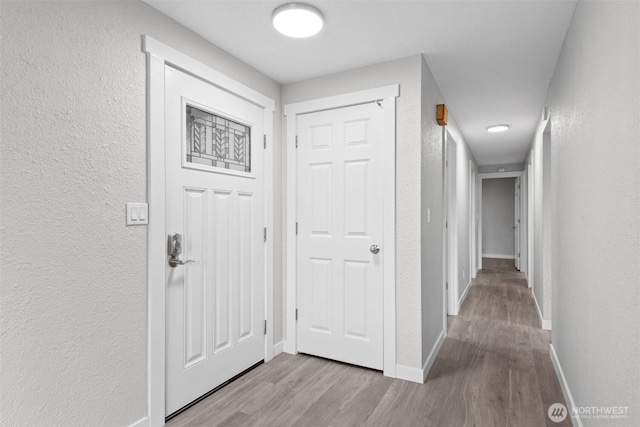 foyer entrance with baseboards, wood finished floors, and a textured wall