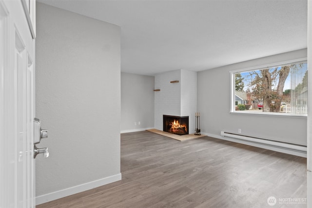 unfurnished living room with a brick fireplace, a baseboard heating unit, baseboards, and wood finished floors