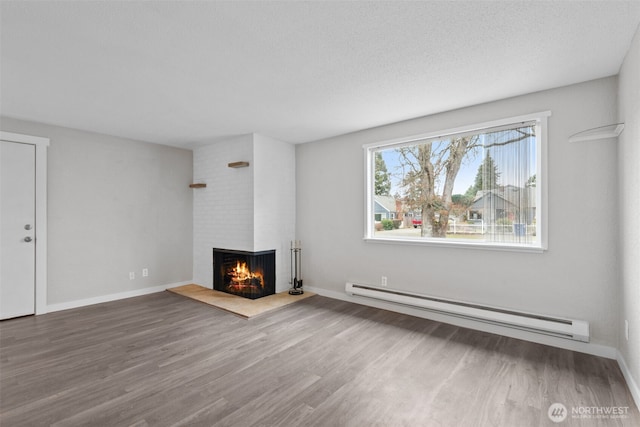 unfurnished living room with a brick fireplace, a baseboard heating unit, baseboards, and wood finished floors