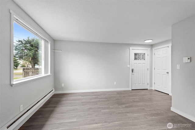 unfurnished living room featuring wood finished floors, baseboards, and a baseboard radiator