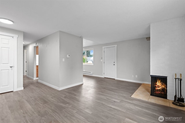 unfurnished living room featuring wood finished floors, a fireplace, baseboards, and baseboard heating