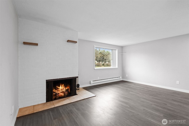 unfurnished living room with baseboard heating, a brick fireplace, baseboards, and wood finished floors