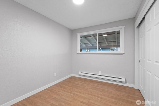 unfurnished bedroom with light wood-style floors, a closet, baseboards, and baseboard heating