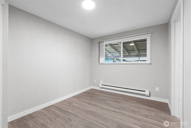 unfurnished room with baseboard heating, baseboards, and wood finished floors