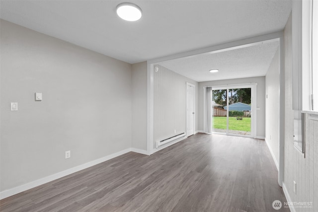 unfurnished room with a baseboard heating unit, baseboards, and wood finished floors