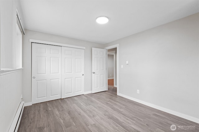 unfurnished bedroom featuring a closet, a baseboard heating unit, baseboards, and wood finished floors