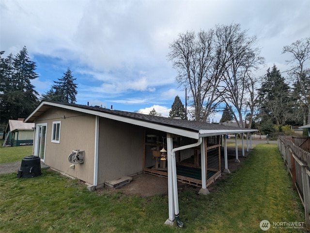 back of house featuring a lawn, an outdoor structure, and fence