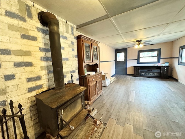 interior space featuring a wood stove, a healthy amount of sunlight, wood finished floors, and a ceiling fan