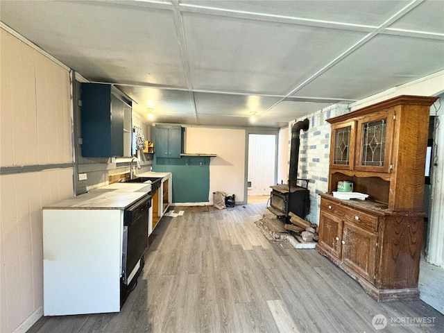 kitchen with dishwasher, light wood-type flooring, light countertops, a wood stove, and a sink