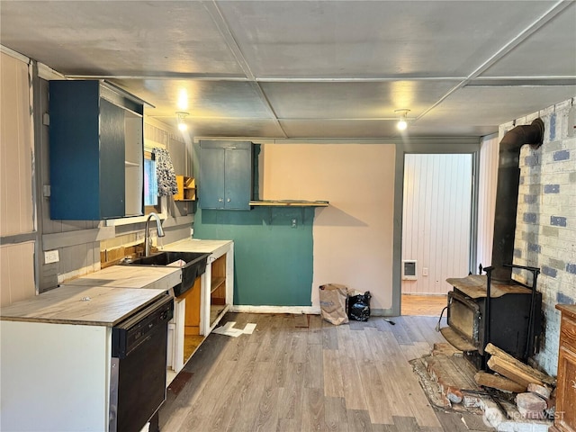 kitchen featuring light countertops, black dishwasher, a wood stove, light wood-style floors, and a sink