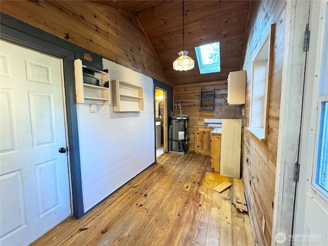 kitchen featuring lofted ceiling with skylight, light wood-style flooring, electric water heater, wood walls, and wooden ceiling