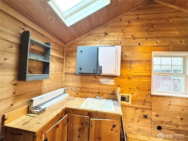 kitchen featuring a sink, lofted ceiling with skylight, wooden walls, and wooden ceiling