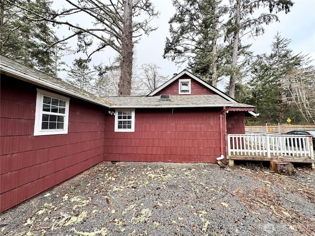 view of property exterior with a deck, fence, and a shingled roof