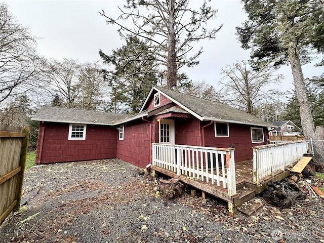 back of property with fence, roof with shingles, and a wooden deck