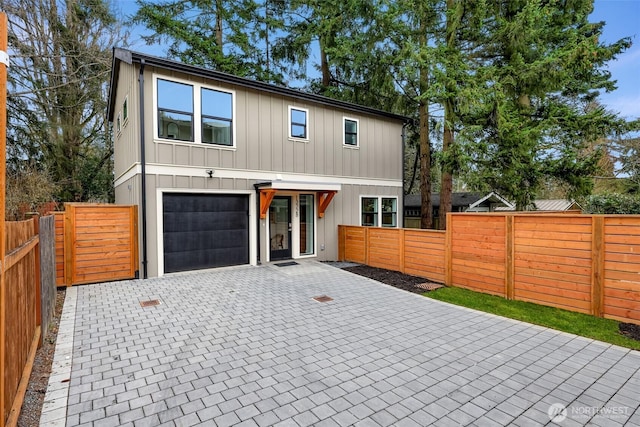 view of front facade featuring decorative driveway, an attached garage, fence private yard, and board and batten siding