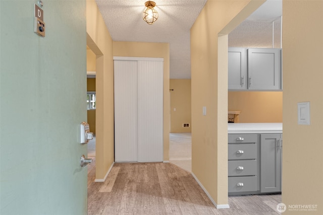 hall featuring baseboards, light wood-style floors, and a textured ceiling