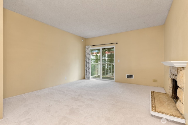 unfurnished living room with visible vents, carpet floors, a textured ceiling, and a stone fireplace