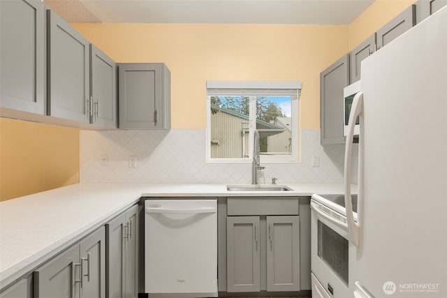 kitchen featuring gray cabinets, a sink, white appliances, light countertops, and decorative backsplash