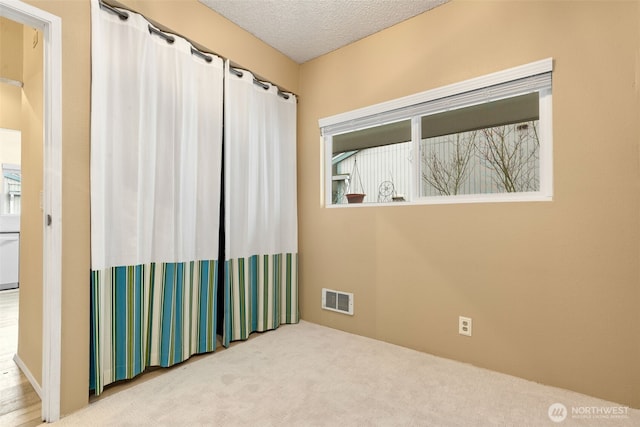 empty room with visible vents, a textured ceiling, and carpet