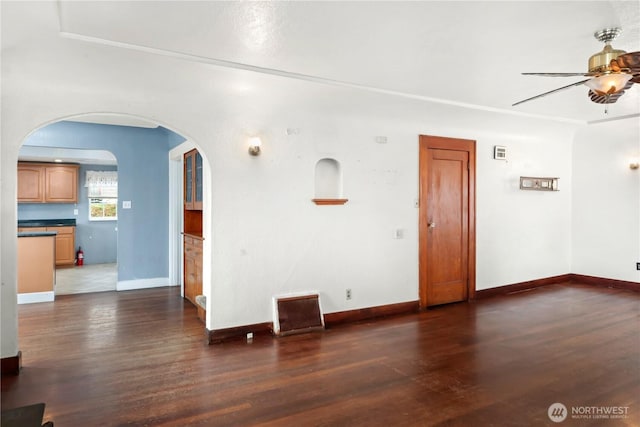 unfurnished living room with arched walkways, baseboards, a ceiling fan, and wood finished floors