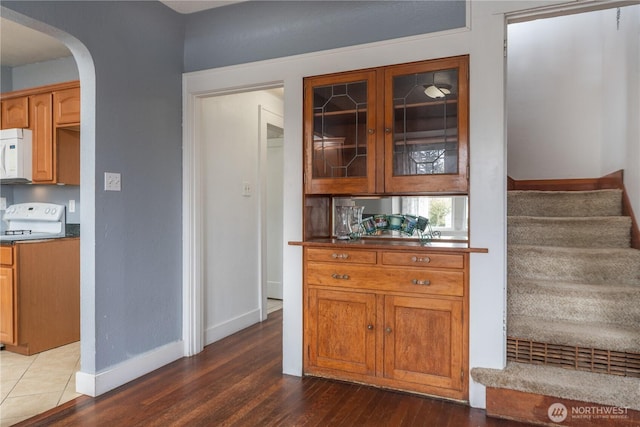 kitchen featuring dark countertops, glass insert cabinets, arched walkways, white appliances, and dark wood-style flooring