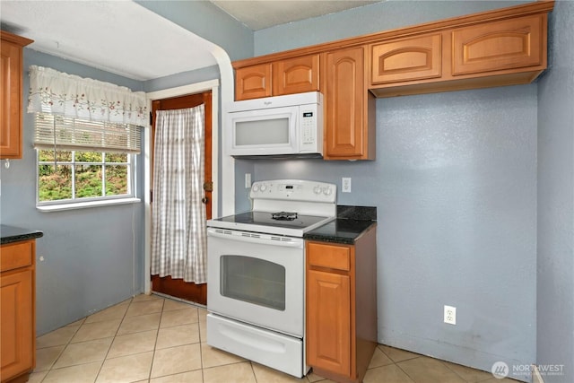 kitchen featuring light tile patterned floors, white appliances, brown cabinets, and dark stone countertops