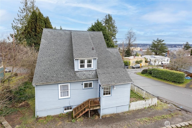 rear view of property featuring fence and roof with shingles