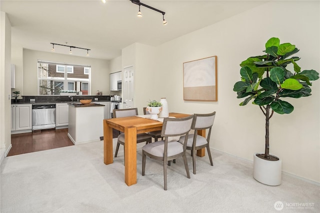 carpeted dining room with track lighting, baseboards, and a sink