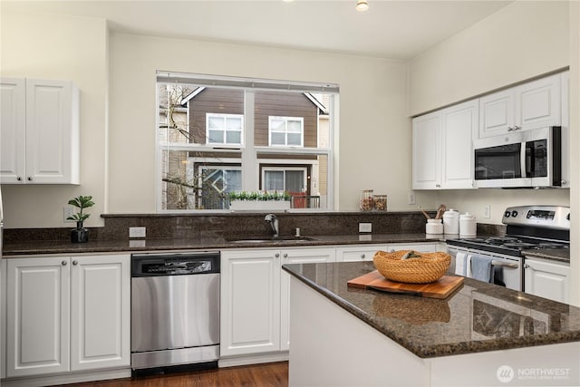 kitchen featuring dark stone countertops, a kitchen island, a sink, stainless steel appliances, and white cabinetry