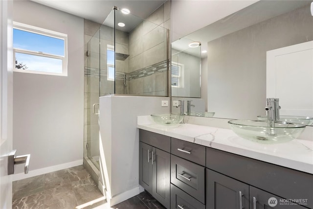 full bathroom featuring a sink, baseboards, double vanity, and a shower stall