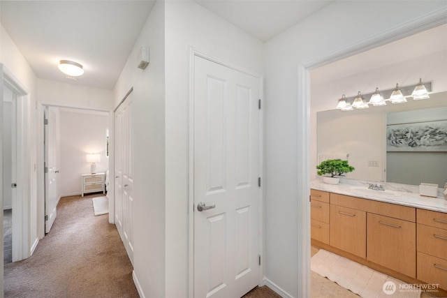 hall with light colored carpet, baseboards, and a sink