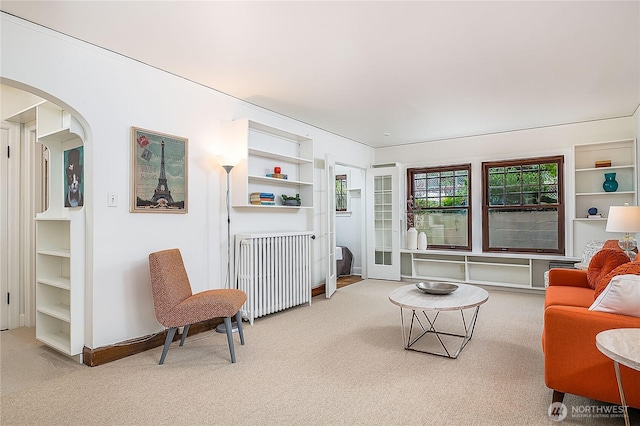 carpeted living room with arched walkways, radiator heating unit, and baseboards