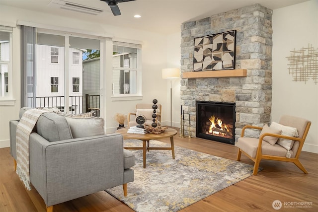 living area featuring a fireplace, wood finished floors, baseboards, and ceiling fan