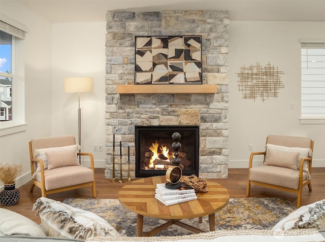 living area featuring baseboards, a stone fireplace, and wood finished floors