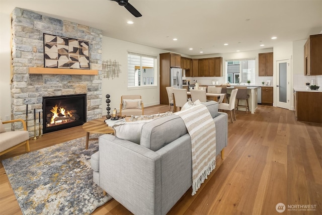 living room featuring a stone fireplace, recessed lighting, a ceiling fan, and light wood-type flooring