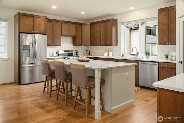 kitchen with a sink, stainless steel appliances, light wood-style floors, backsplash, and a center island