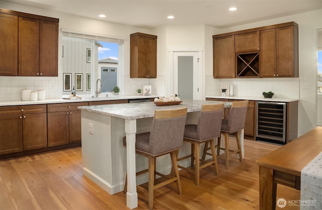 kitchen with light wood finished floors, backsplash, a center island, wine cooler, and a breakfast bar